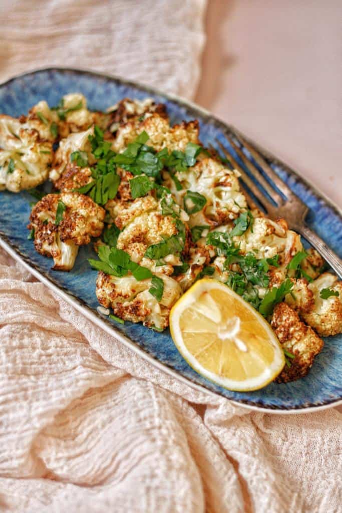 amazing golden crispy texture of air fried cauliflower drizzled with tahini sauce dressing served with lemon cutlets and  finely chopped fresh parsley on the top