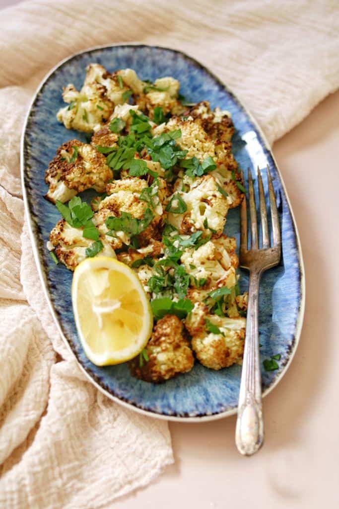 crispy golden air fried cauliflower garnished with finely chopped fresh parsley along side lemon cutlets ready to be served