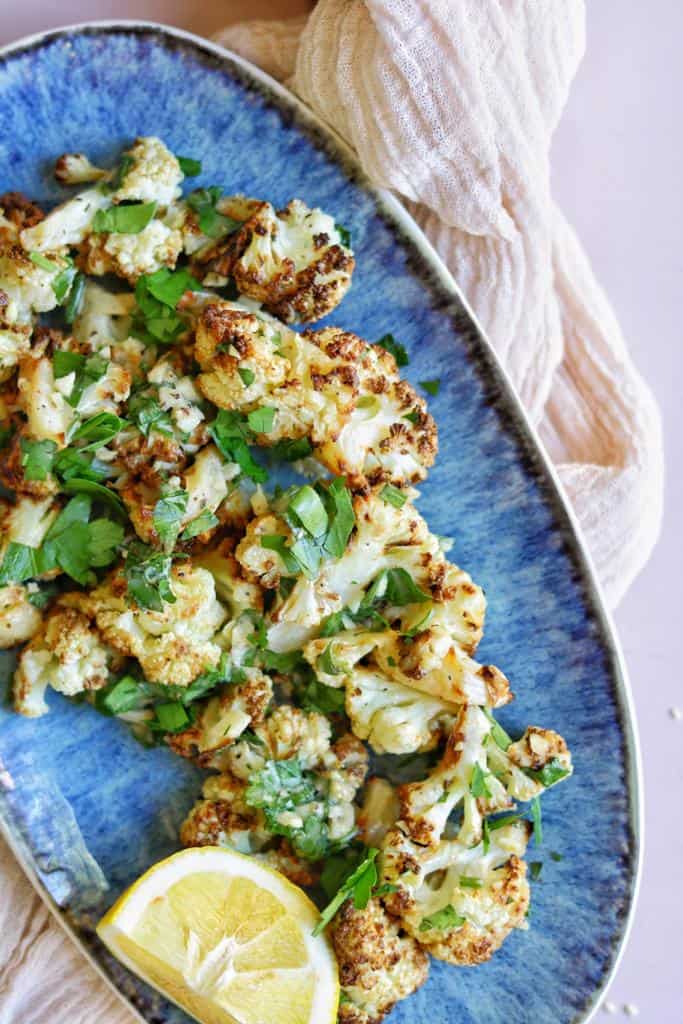 air fried cauliflower with tahini sauce dressing and lemon cutlets topped with finely chopped fresh parsley 