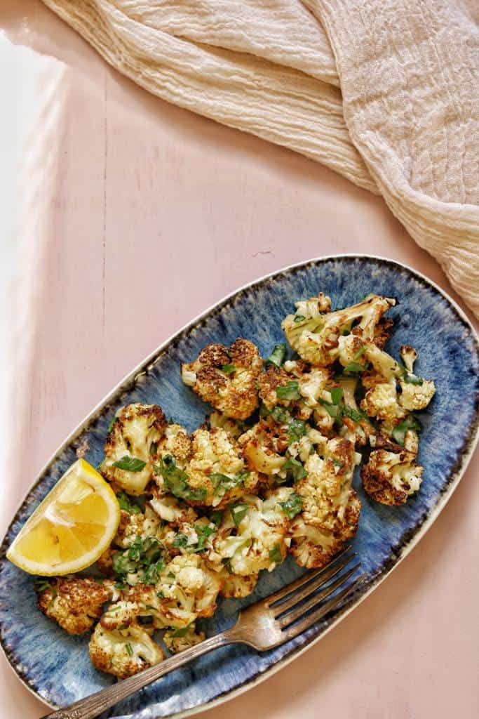golden crispy cauliflower garnished with finely chopped soft parsley on the top served with fresh lemon cutlets 