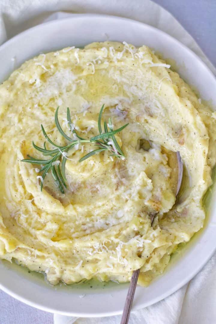 a hearty yukon gold mashed potatoes skin on topped with freshly grated parmesan cheese, olive oil, and rosemary fresh herb