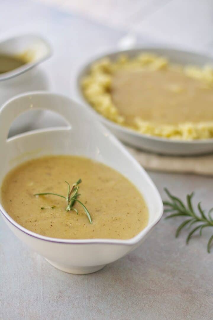 A bowl of tasty vegetarian gravy decorated with rosemary has onion, garlic fried in butter and flour to male a roux that thickens your vegetable broth.
