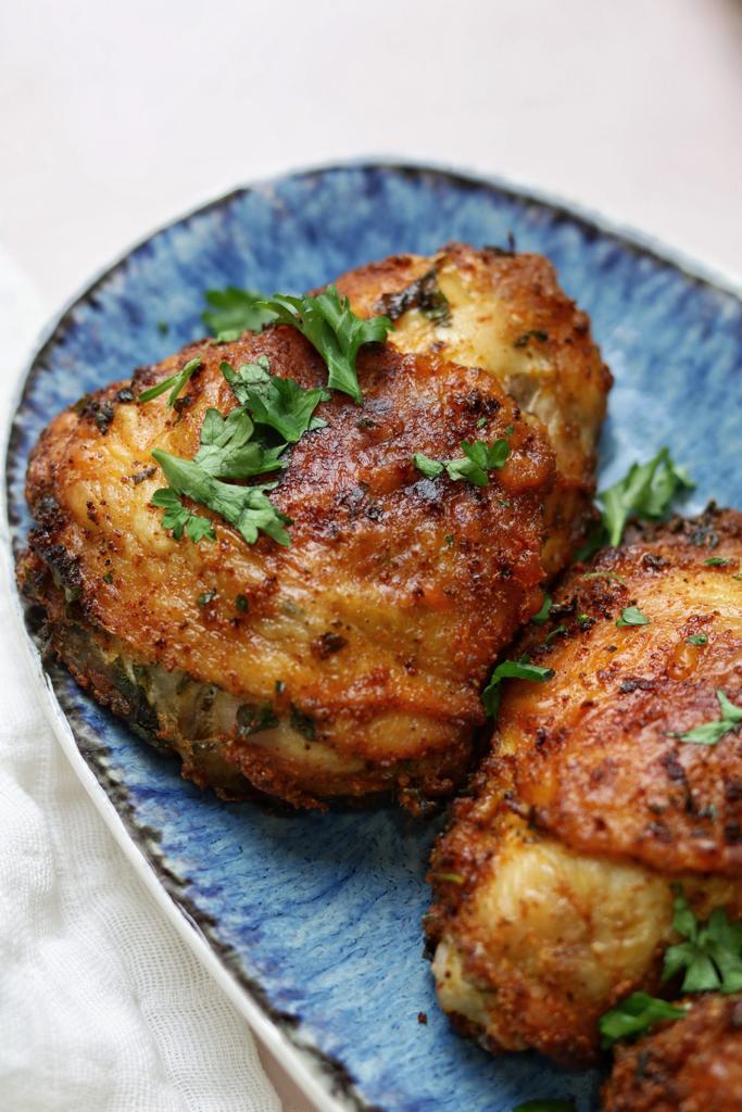 Air fryer bone in chicken thighs with crispy skin on the outside and tender juiciness on the inside, served with finely chopped fresh parsley on the top.