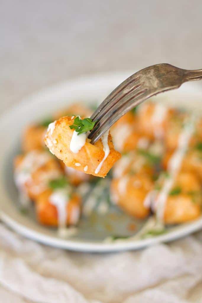 Cubed air fryer salmon nuggets with a white sauce on top and garnished with parsley.