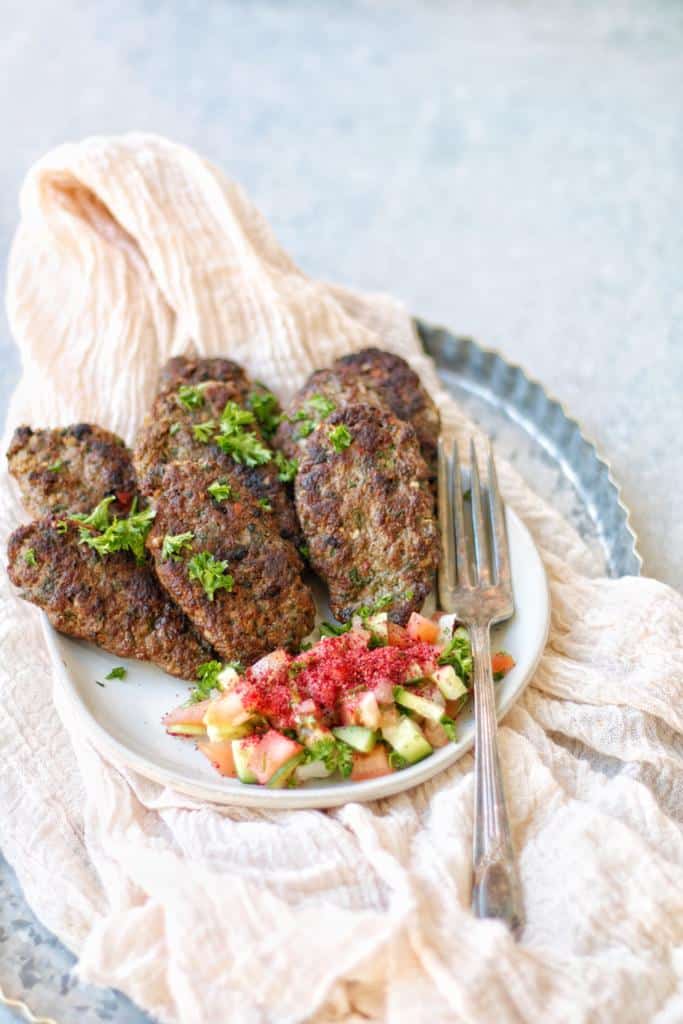 cooked kafta kabobs garnished with finely chopped fresh parsley and served with lebanese fattoush salad