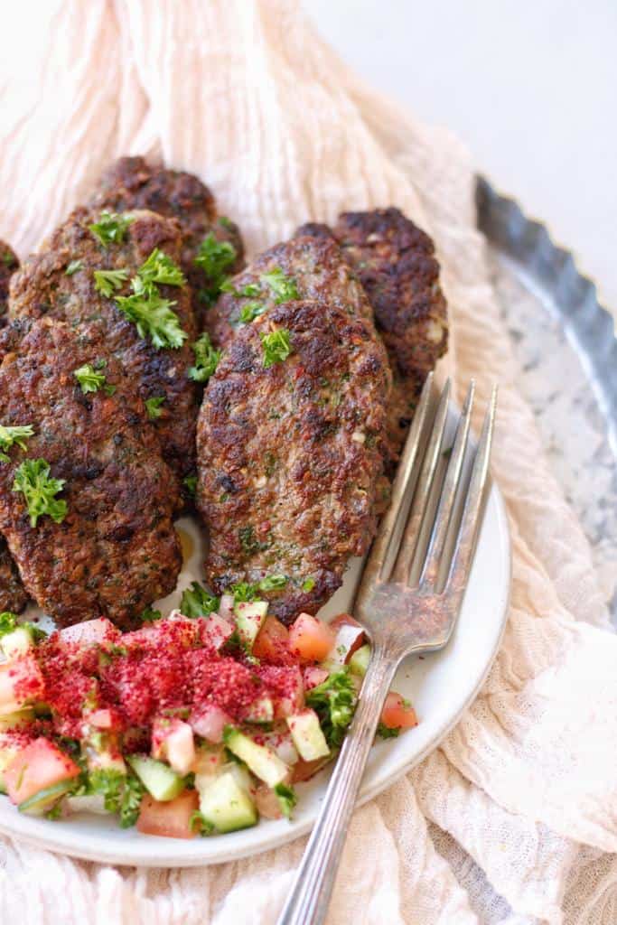 cooked kafta kabobs made up with ground beef and spices garnished with finely chopped fresh parsley and served with lebanese fattoush salad