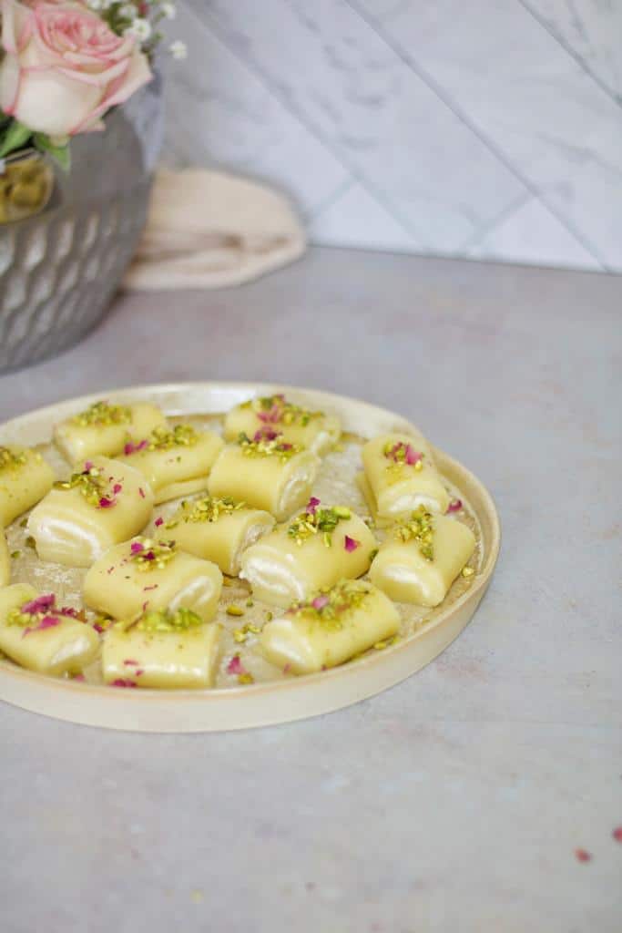 middle eastern halawet el jibn is a delectable sweet cheesy rolls that melt-in-the-mouth! They are stuffed with Ashta cream, crowned with rosebuds, and drizzled with a sweet syrup.
