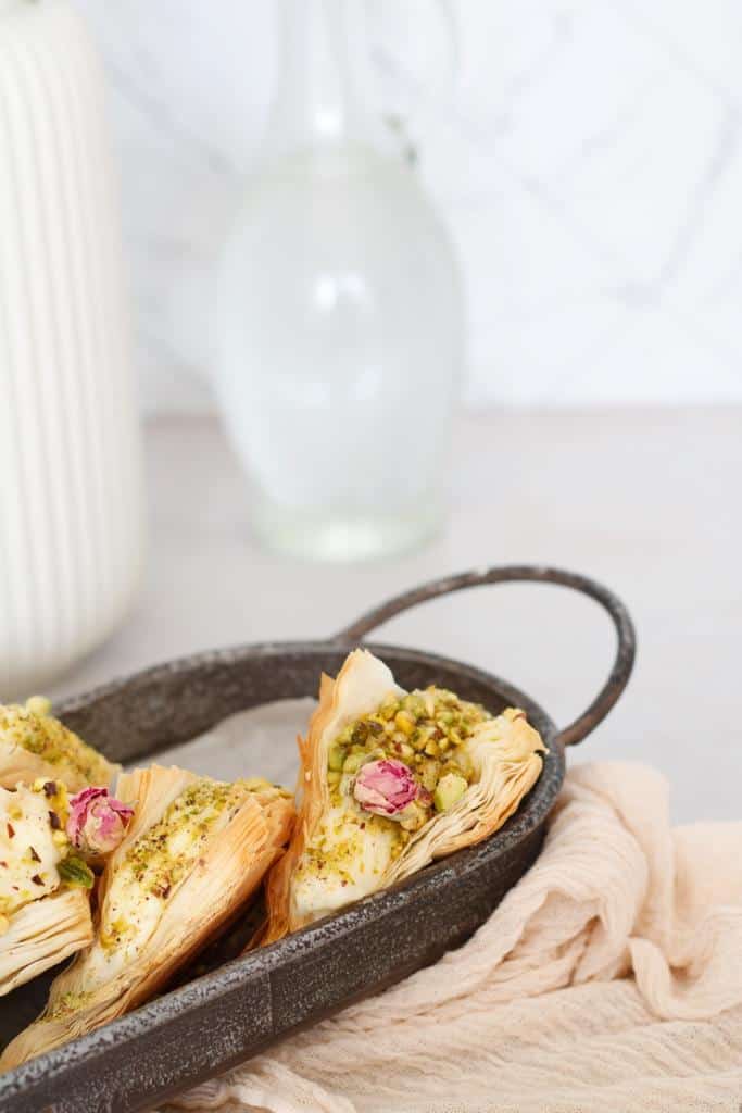 layers of crispy phyllo dough, warbat bil ashta are filled with Ashta, garnished with crushed pistachios, drizzled with a simple syrup, and topped with rosebuds