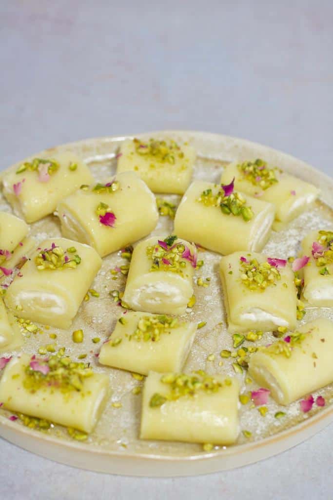 Sweet cheese rolls are soft sweet cheese dough, stuffed with Ashta cream, topped with crushed pistachios, and drizzled with a sweet syrup.