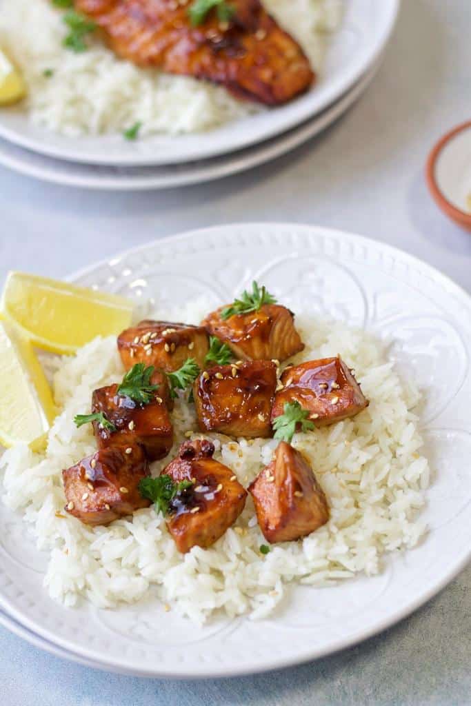 salmon bites served on a bed of rice garnished with finely chopped fresh parsley alongside lemon cutlets