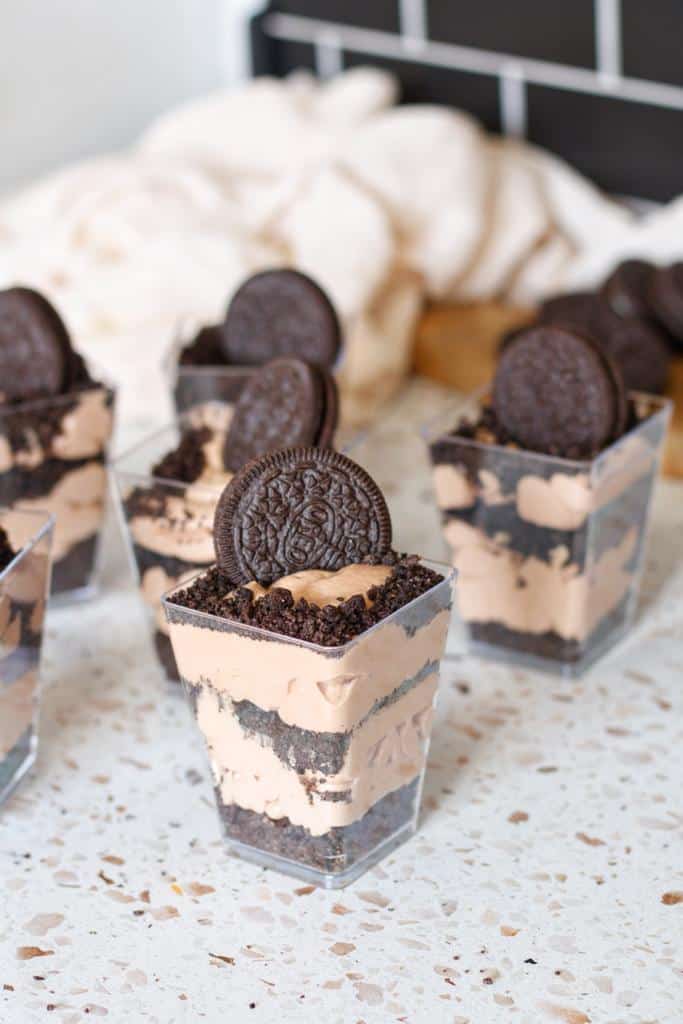 Alternating layers of crushed Oreos and chocolate whipped cream prepared in mini rectangular cups and topped with an Oreo cookie and crumbs.