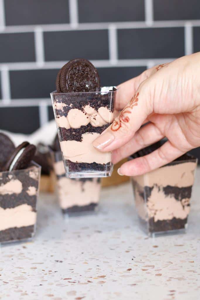 Alternating layers of crushed Oreos and chocolate whipped cream prepared in mini rectangular cups and topped with an Oreo cookie and crumbs.