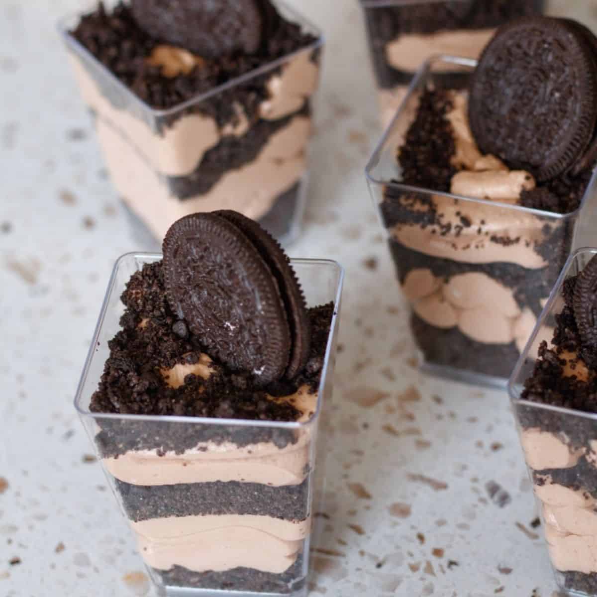 No Bake Oreo dessert cups with alternating layers of crushed Oreos and chocolate whipped cream topped with an Oreo cookie and crumbs