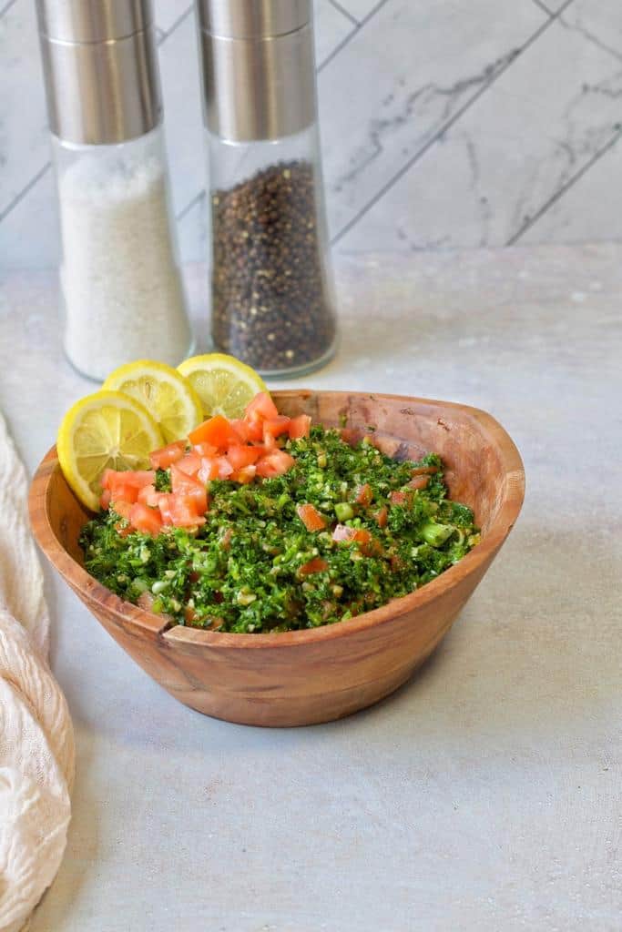 Low carb tabouli salad served in w wooden ball with chopped tomatoes on top and lemon slices.