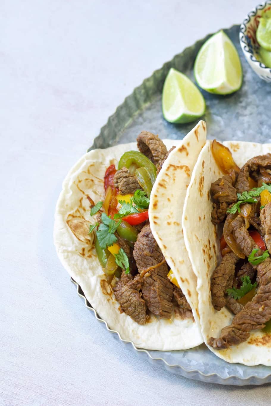 low-carb tortillas filled with cooked skirt steak, onions, green, red, and yellow bell peppers and served with lime wedges
