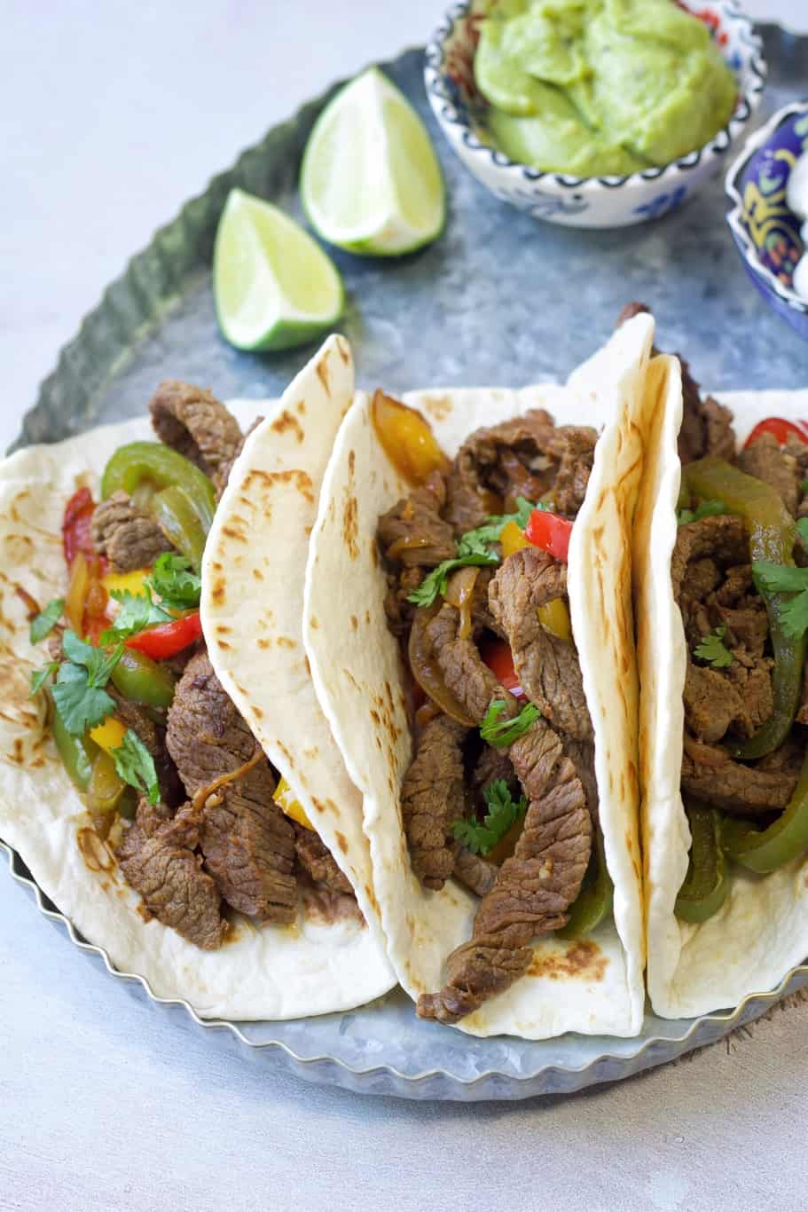 keto steak fajita tortillas made up of cooked skirt steak, onions, and bell peppers, sprinkled with chopped cilantro, and served with lime wedges and guacamole
