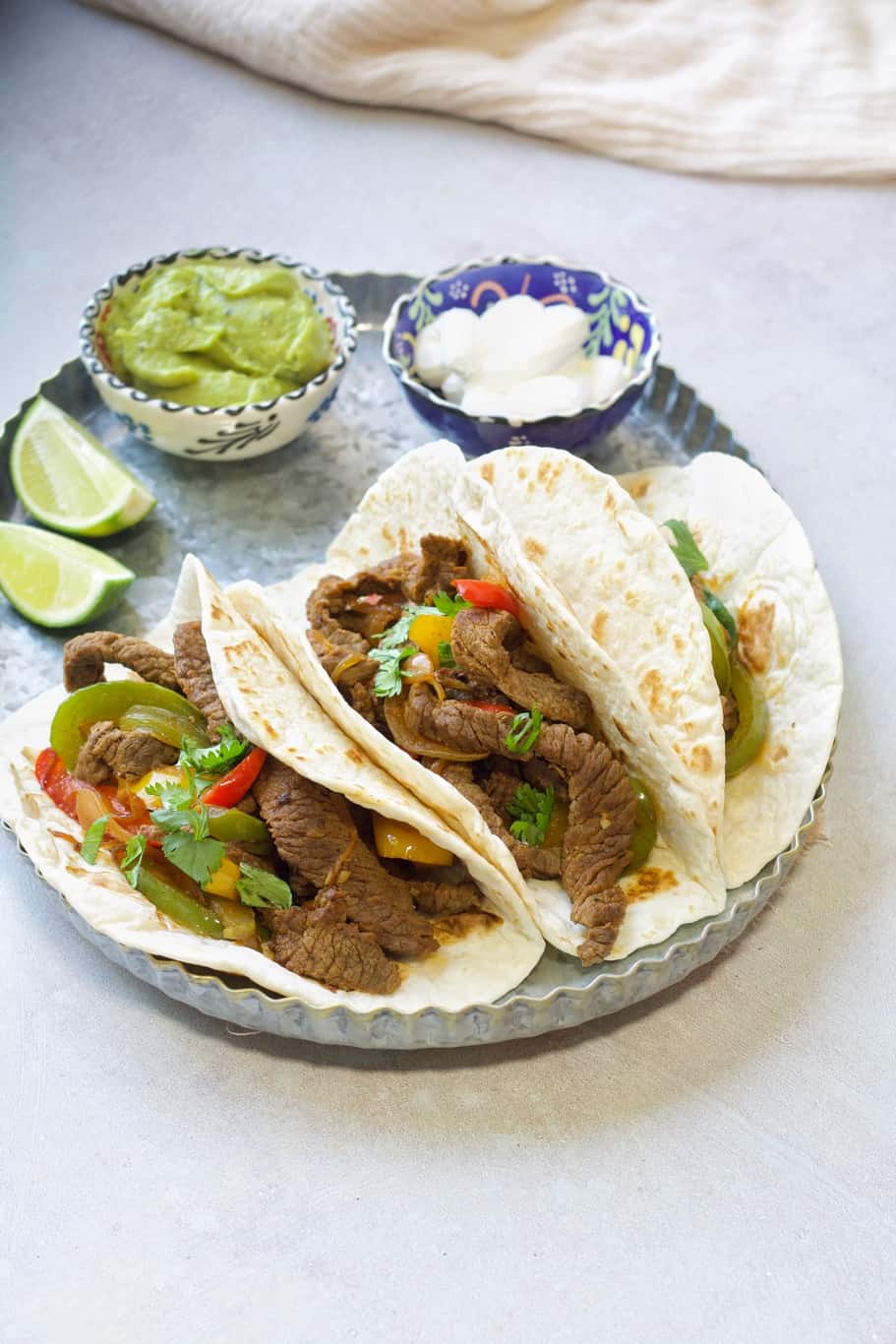 warm low-carb tortillas filled with keto beef fajitas served with lime wedges, guacamole, and sour cream