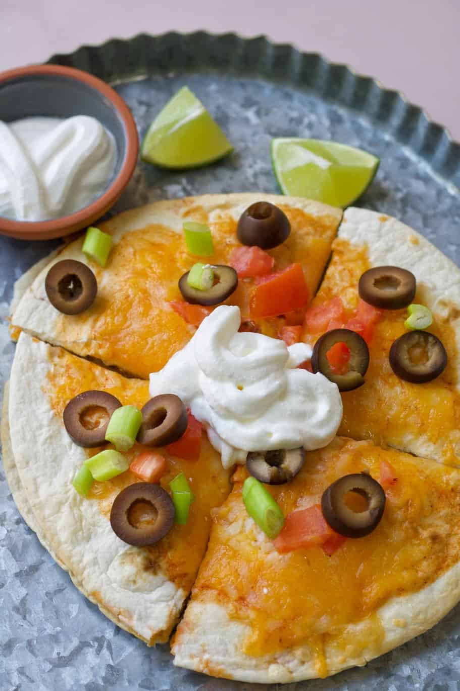 Delicious taco bell pizza topped with olives, green onions, enchilada sauce, roma tomatoes and sour cream