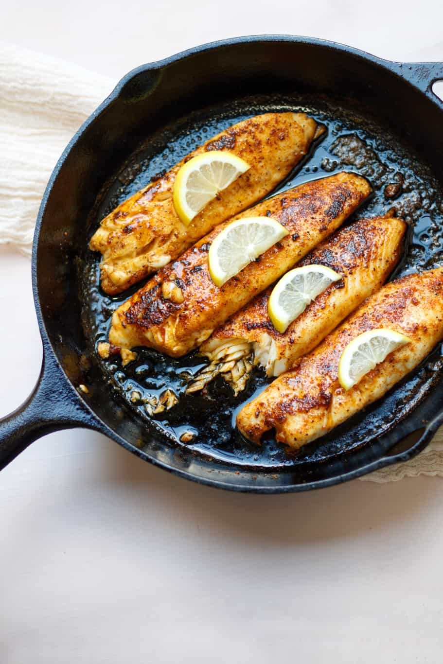 four lemon butter tilapia filets topped with lemon slices in a cast iron skillet