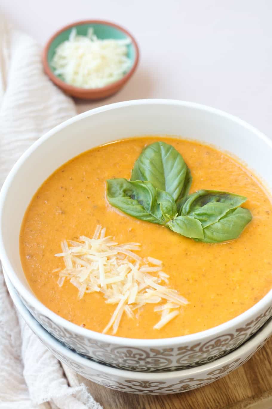 a warm and cozy creamy tomato basil soup with parmesan served with  fresh basil leaves and grated parmesan cheese on the top. 