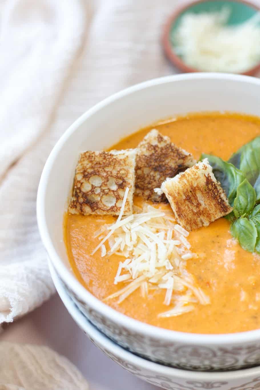 This soup with heavy cream is served with fresh basil leaves, grated parmesan cheese, and crunch croutons on the top.