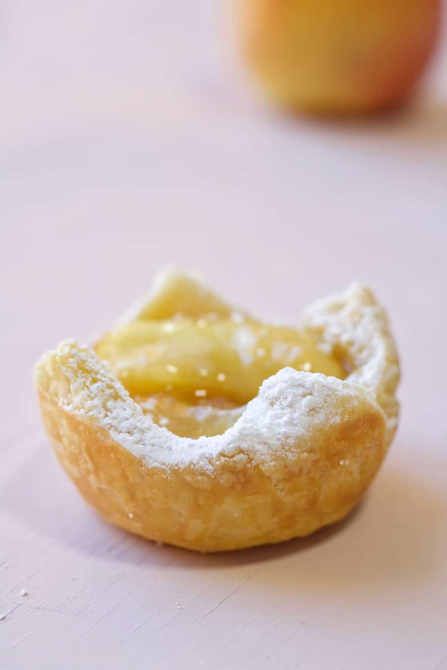 a mini apple tart made with puff pastry and sweet apple filling and served with powdered white sugar on its golden flaky edges