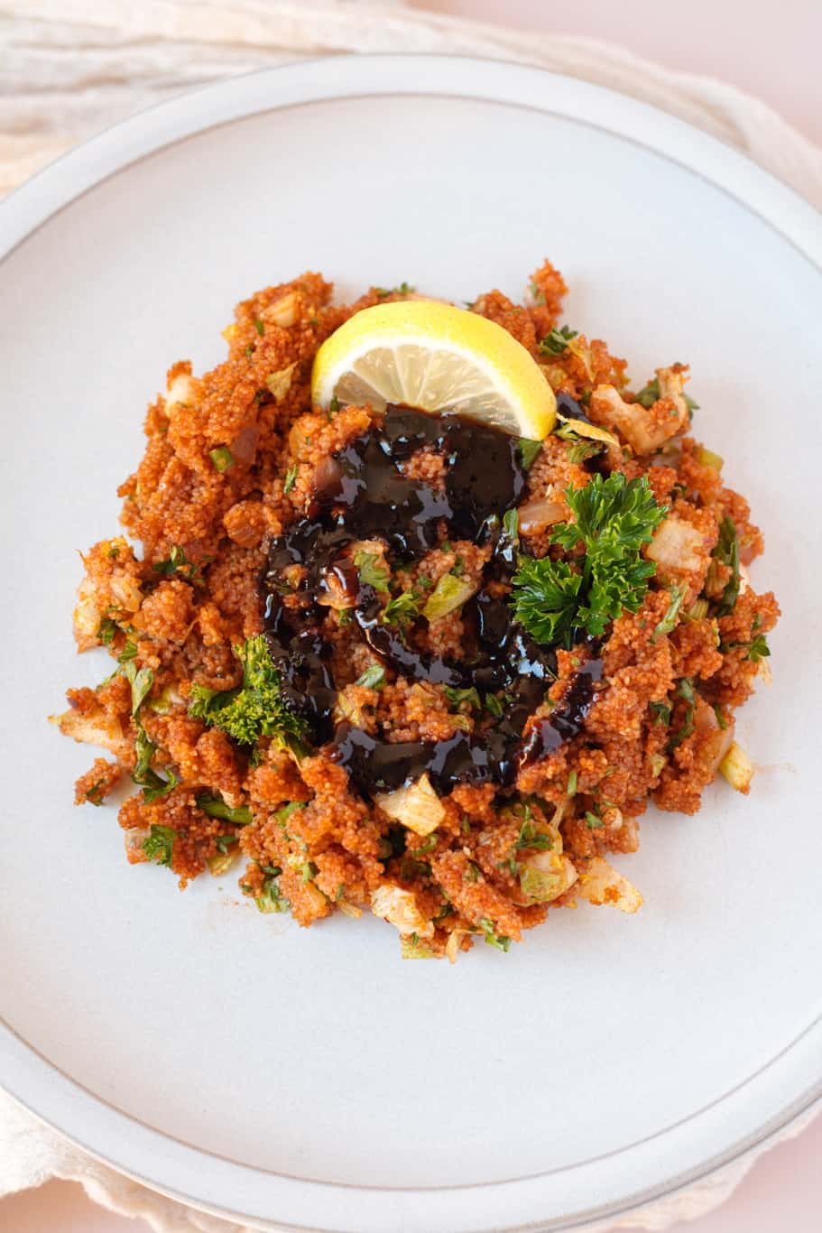 Kisir salad topped with a drizzle of pomengerate molasses, a lemon wedge, and parsley.