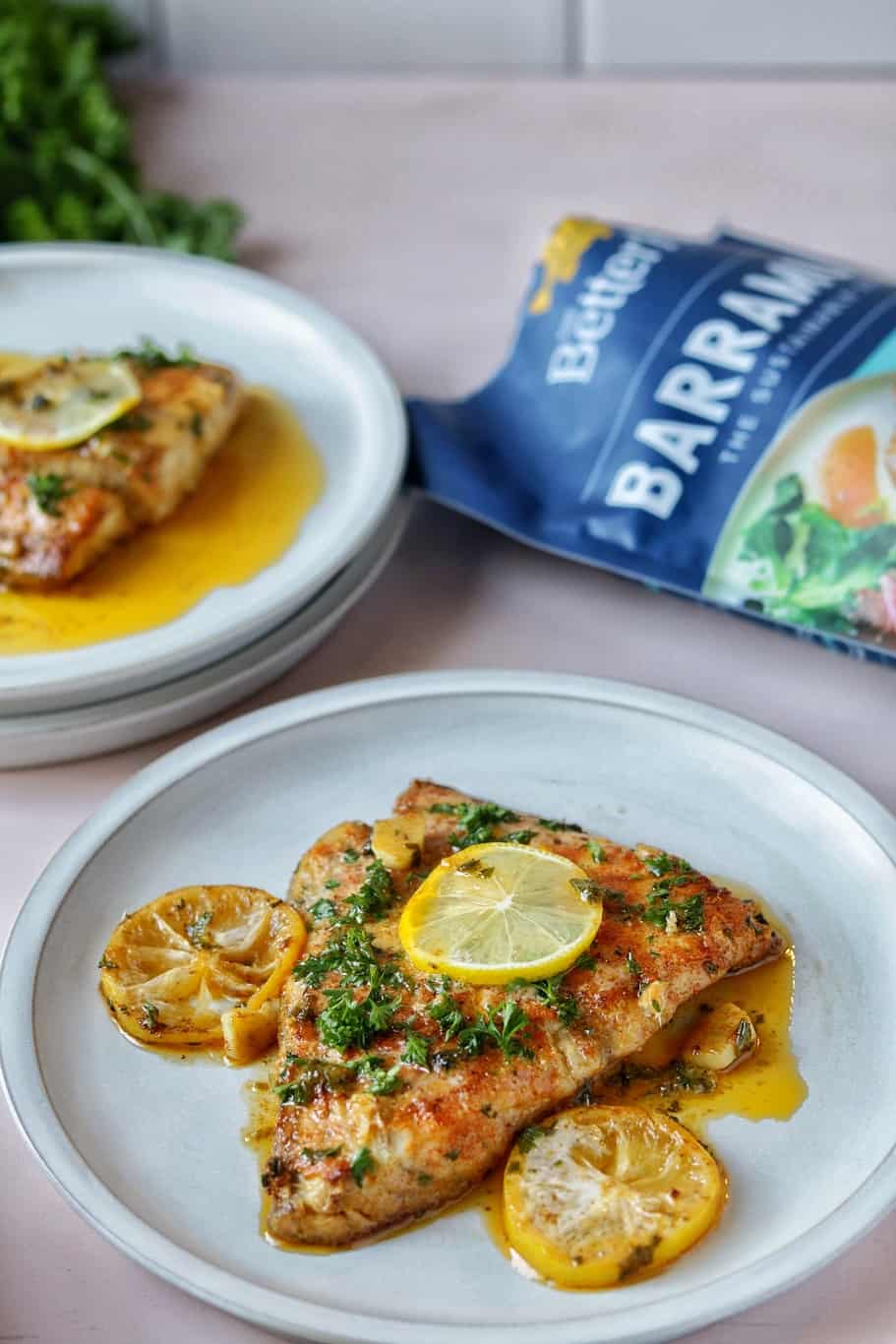 flaky barramundi fillets with crispy skin served with lemon butter sauce, finely chopped parsley, and lemon wedges