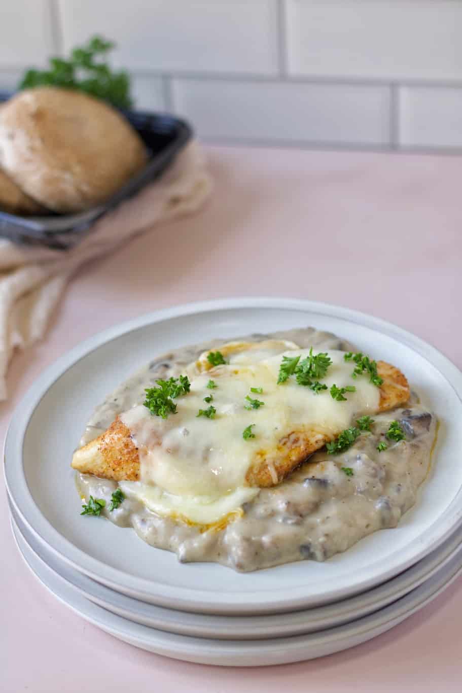 a slice of chicken breast swimming in a creamy mushroom sauce, topped with cheese, and garnished with parsley.