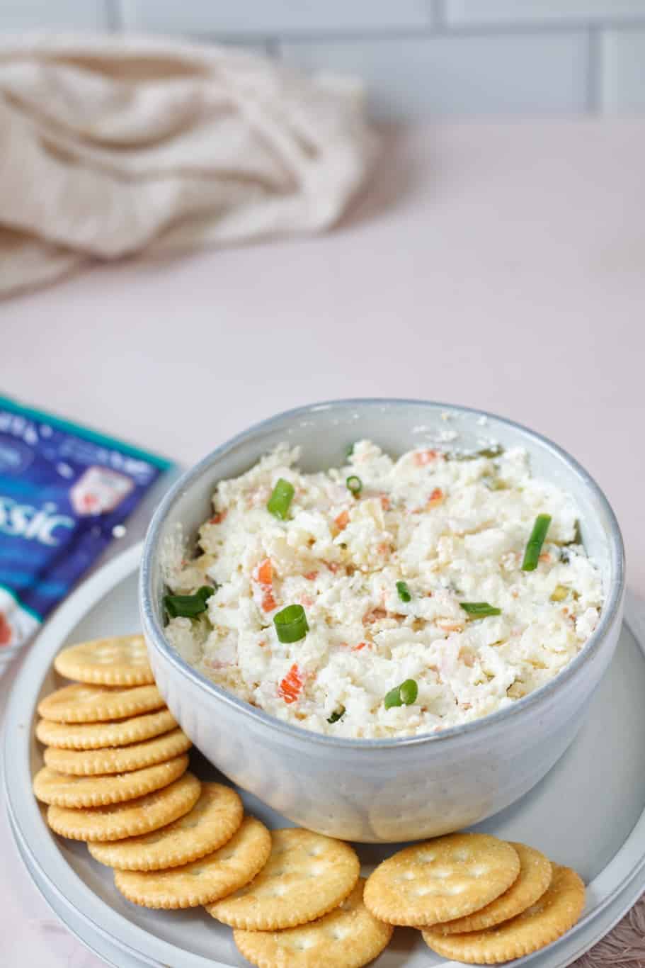 A bowl of philadelphia cheese crab dip garnished with green onions and served with crackers