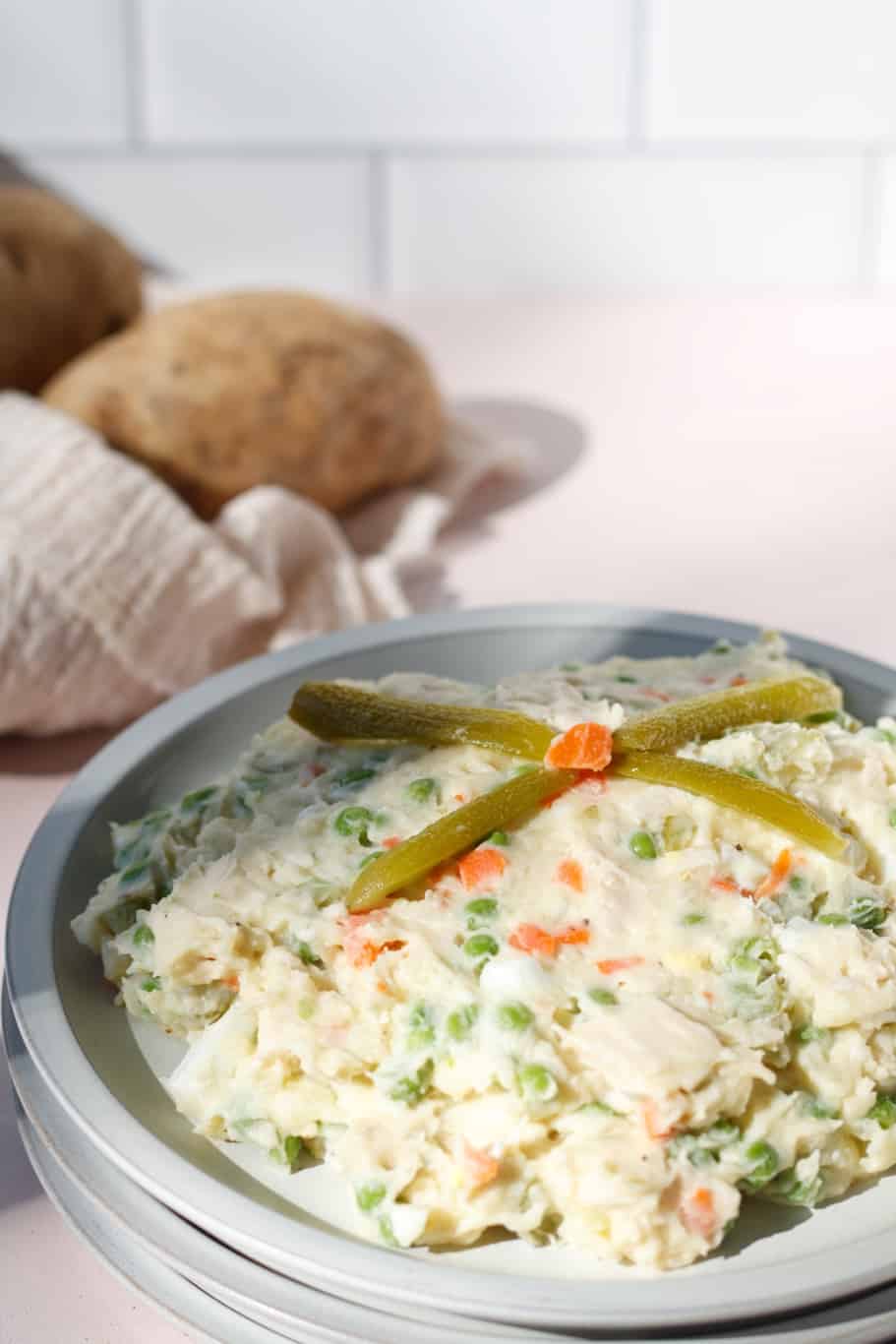 A plate of creamy tangy salad olivieh made up of cooked chicken, potatoes, eggs, and other veggies. It is served with dill pickles on the top.