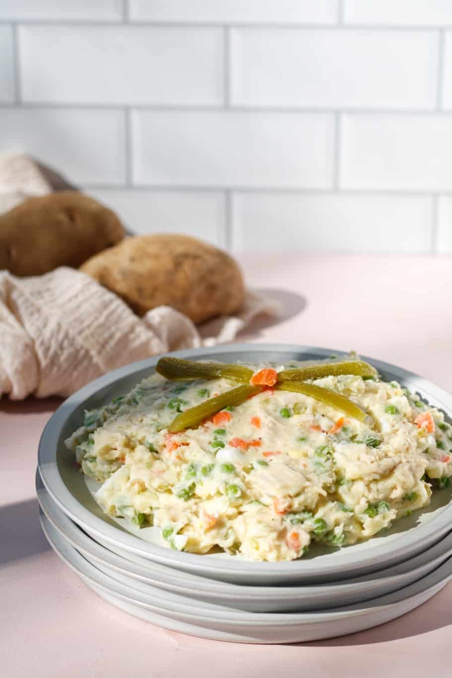 salad olivieh made up of cooked chicken, potatoes, eggs, and green peas and diced boiled carrots. It is served with pickles on the top. Alongside the dish, there are 2  medium russet potatoes.