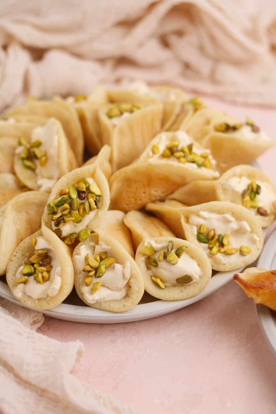 a plate of qatayef asafiri stuffed with sweetened ashta filling and topped with crushed pistachios ready to be served