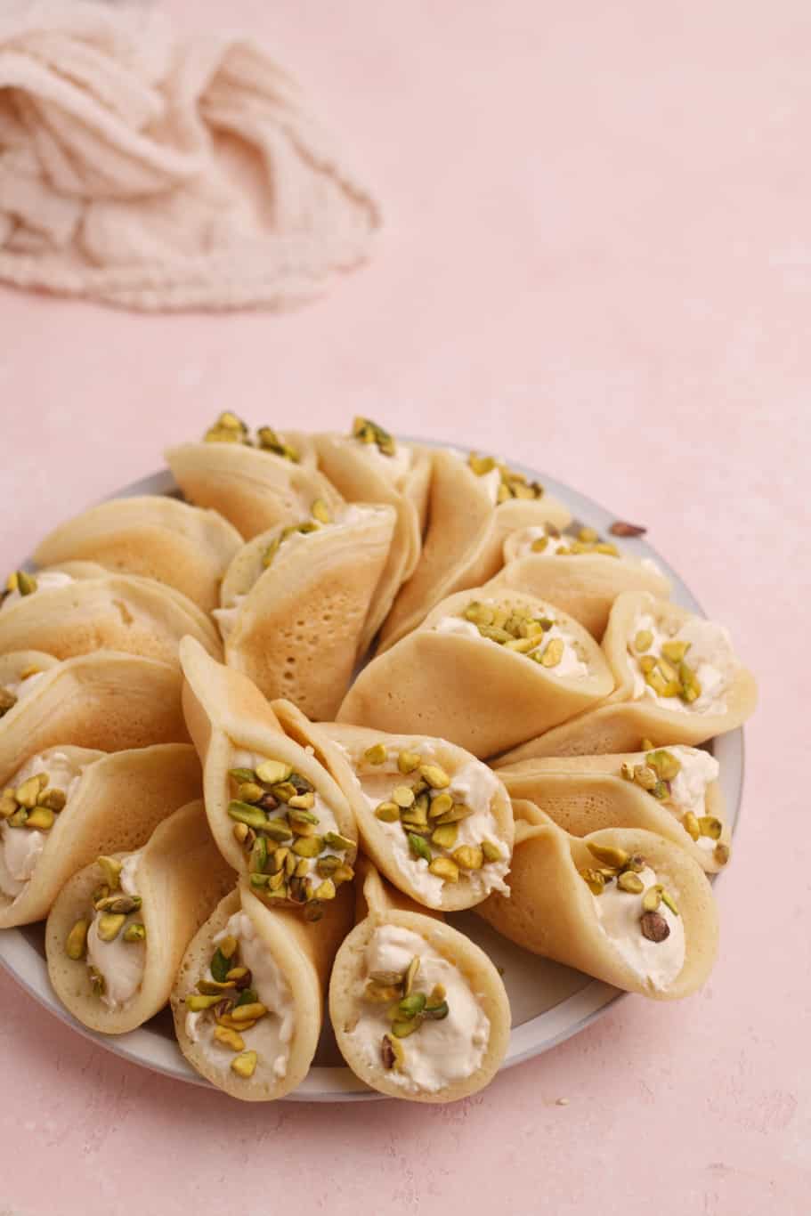 a plate of atayef pancake filled with clotted ashta cream and topped with crushed pistachios ready to be served
