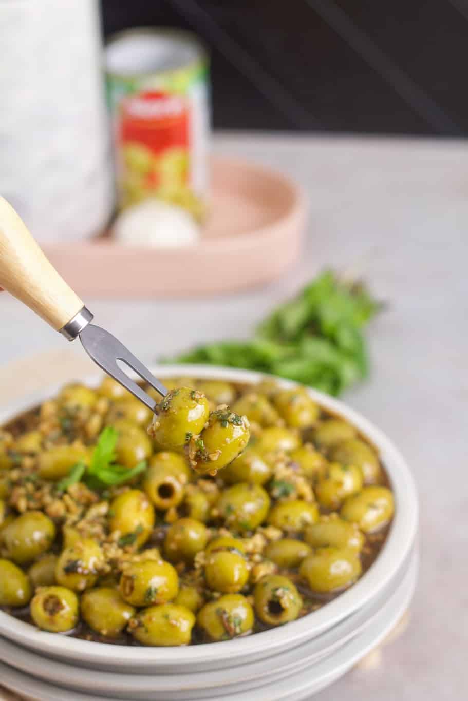 A fork that holds two zeytoon parvardeh that are marinated in a mixture of olive oil, chopped walnuts, pomegranate molasses, garlic, and chopped fresh mint.