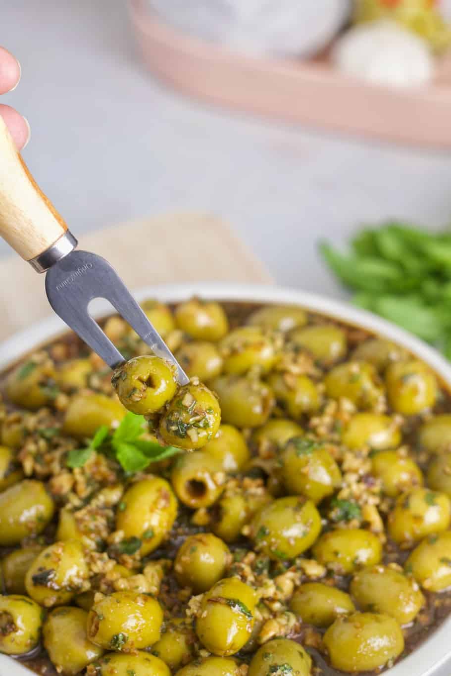A fork with two Persian marinated olives. The olives are served in a medium bowl with a plenty of marinade dressing.