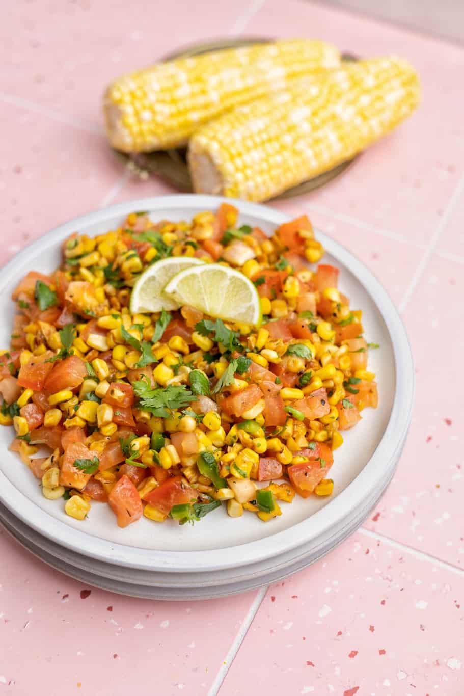 a plate of corn salsa with tomatoes served with lime wedges on the top