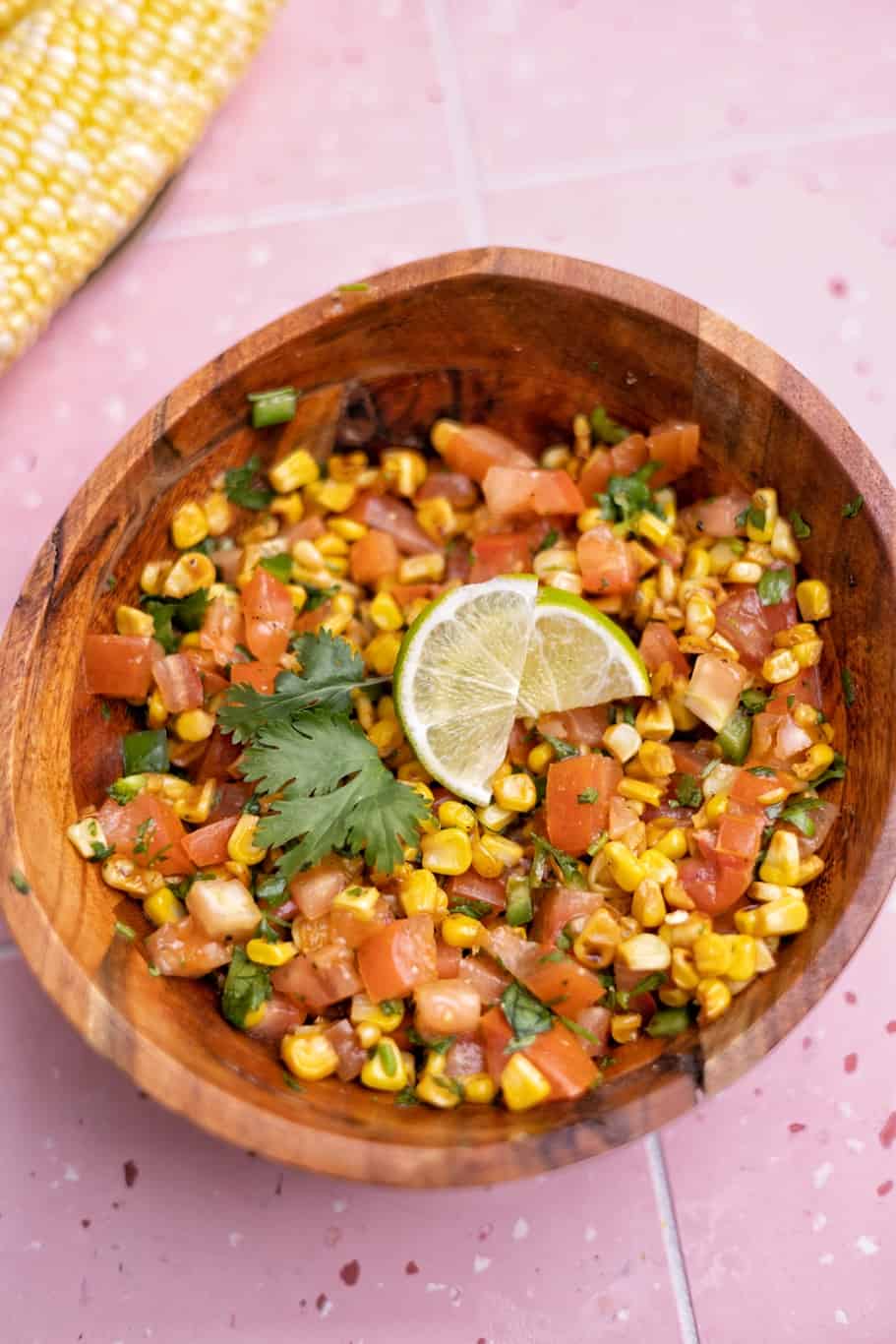 a bowl of charred corn salsa made up of a combination of charred corn, tomatoes, fresh cilantro, lime juice, and spices and served with lemon wedges on the top