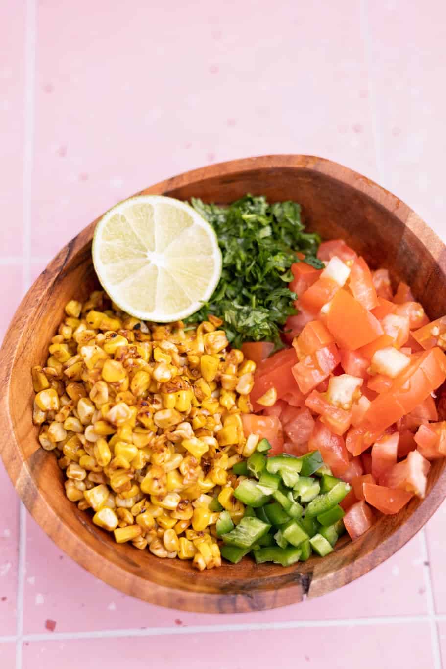 a bowl of charred corn, chopped tomatoes, chopped cilantro, chopped jalapeño, and a lime wedge