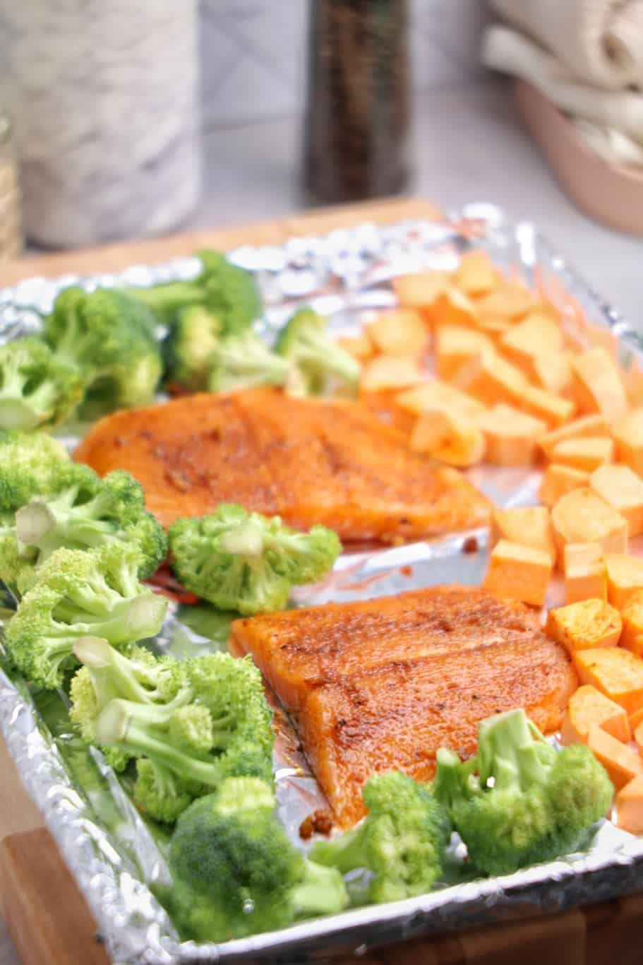 raw salmon with broccoli and cubed sweet potatoes in the sheet pan