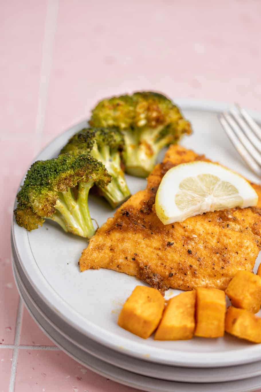 salmon filet served with sweet potatoes, broccoli, and a lemon slice served on a white dish