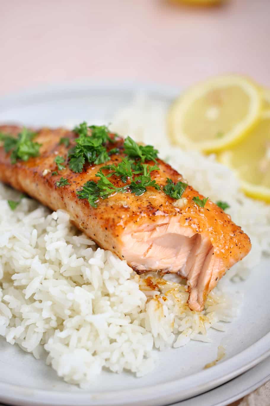 a plate of white rice topped with flaky honey butter salmon garnished with parsley