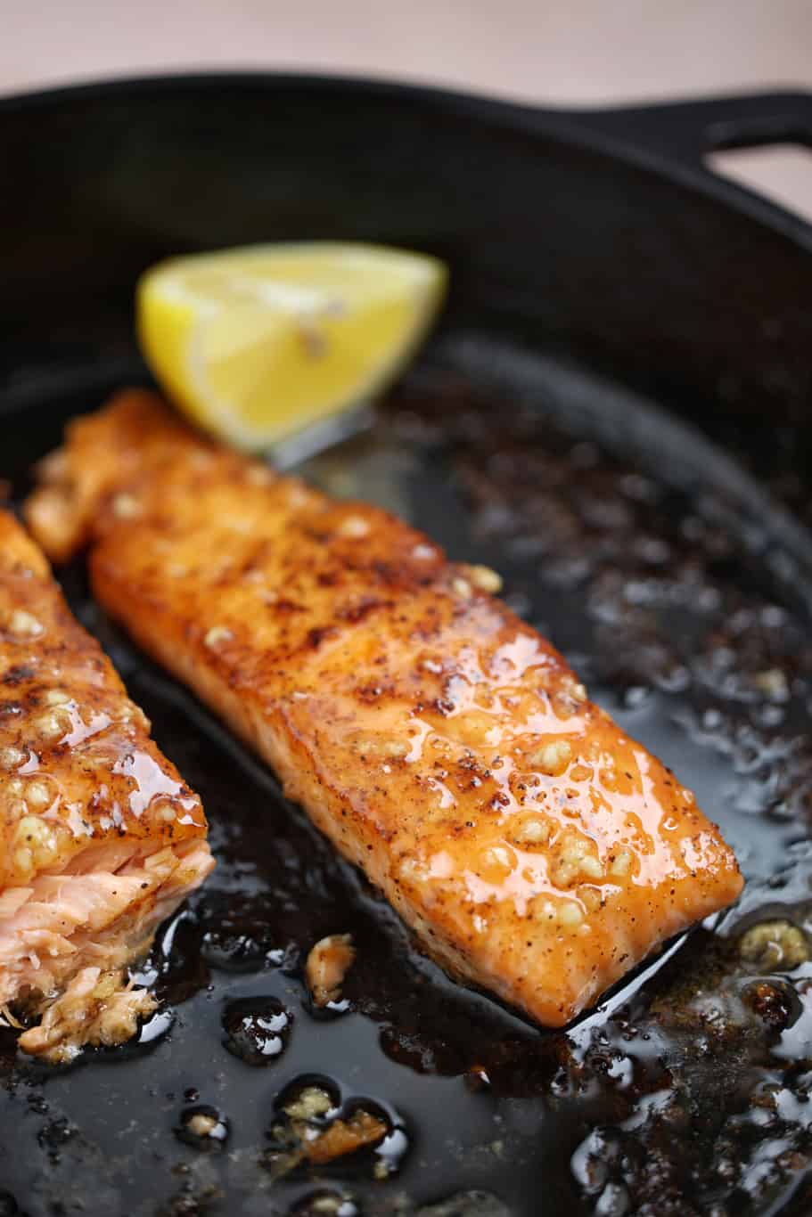 2 pieces of salmon filets seasoned with cajun spices and a piece of lemon in a cast iron skillet 