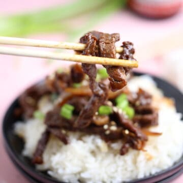 w piece of tender beef held between two chopsticks over a bed of white rice